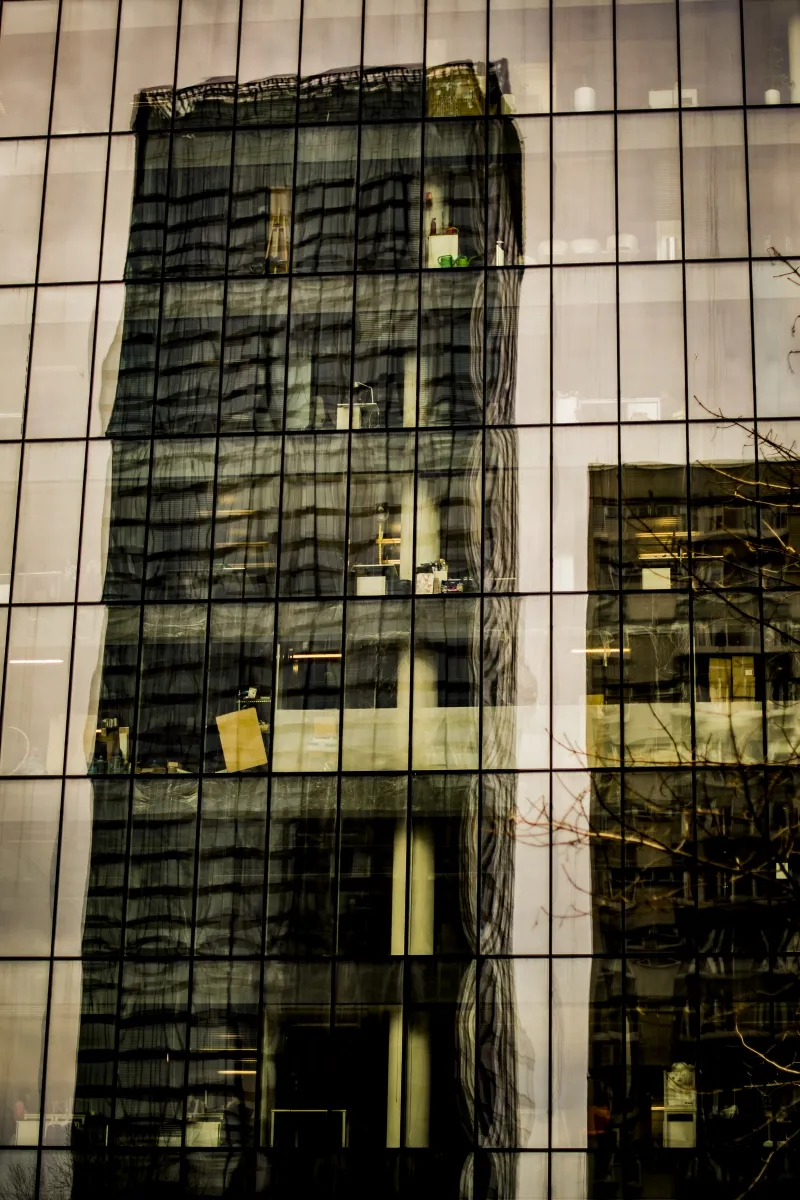 Lit office tower reflected in the glass of a neighboring skyscraper